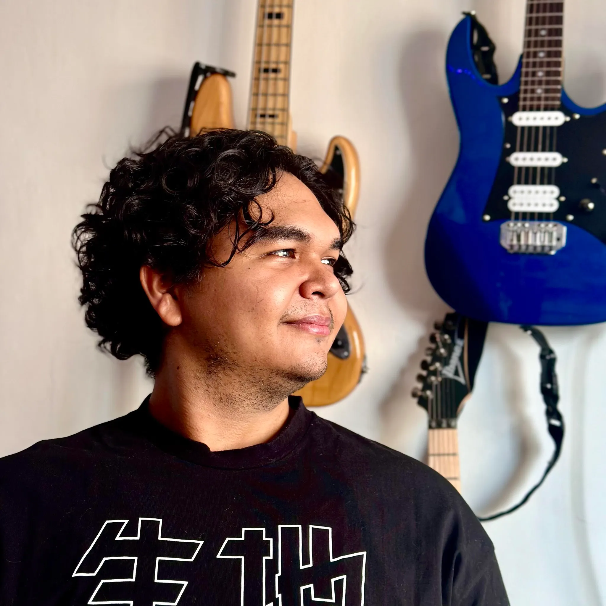 Mateo Gregory in profile with a background of musical instruments such as guitars and a bass.